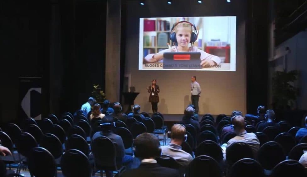 Plenumssal med publikum i headset og en person på storskjerm